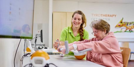 Eine Therapeutin unterstützt die Patientin bei der Armtherapie